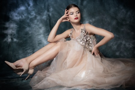 A full length portrait of a mysterious lady in a light beige dress posing indoor. Fairy tale, beauty, fashion.の写真素材