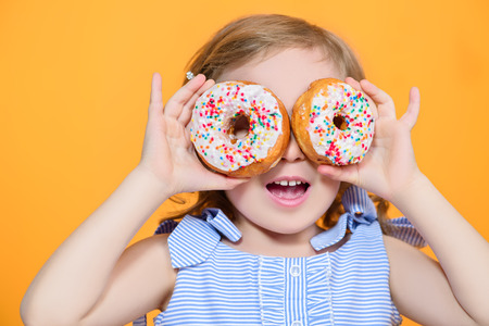 A portrait of a pretty girl with donuts in the studio over the yellow background. Kids, beauty, food, sweets.の写真素材