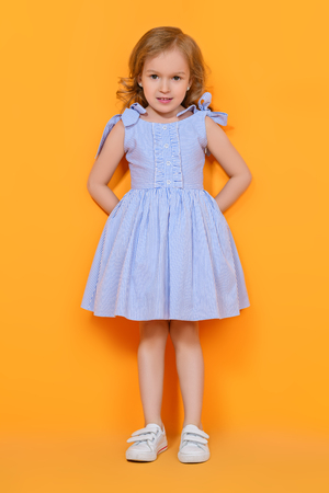 A full length portrait of a pretty girl in a blue dress posing in the studio over the yellow background. Kids, fashion, beauty.の写真素材