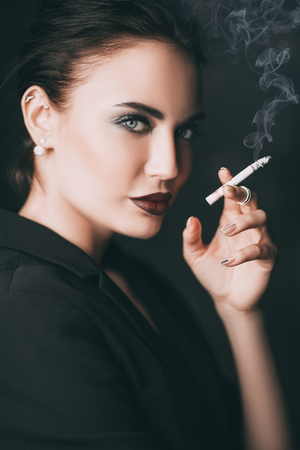 A portrait of a beautiful sexy woman wearing a black blazer smoking cigarette. Fashion, style, beauty.の写真素材