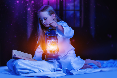 A portrait of a young pretty girl with a lantern and a book. Reading, pajamas.の写真素材