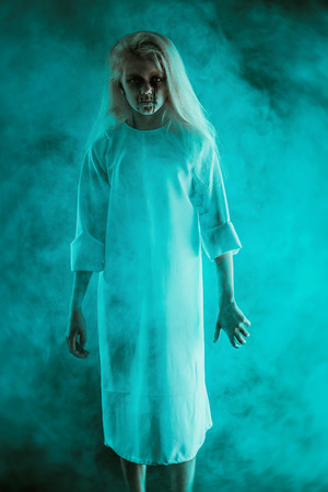A portrait of a scary pale girl from horror film in a fog. Zombie, halloween.の写真素材