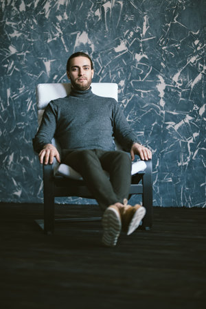 A full length portrait of a handsome stylish man sitting in the armchair. Fashion for men.