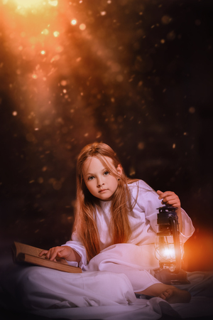 A portrait of a surprised young pretty girl with a lantern and a book. Reading, pajamas.の写真素材