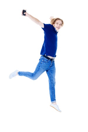 A full length portrait of a young active jumping man with a smartphone posing in the studio over the white background. Casual men fashion.の写真素材