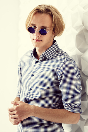 A portrait of a young cool  man in a checked shirt and sunglasses posing indoor. Men fashion, beauty, optics.の写真素材