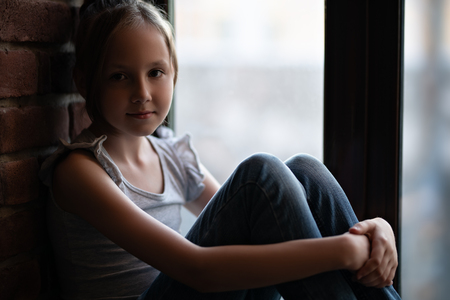 A portrait of a young cute girl over the window in a room. Beauty, summer casual fashion.の写真素材