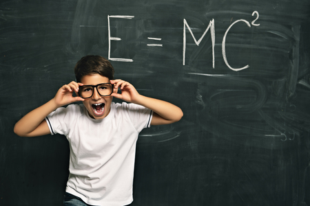 A portrait of a laughing young schoolboy over the blackboard in a classroom. Beauty, fashion, school, education.の写真素材