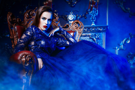 A charming vampire lady is sitting at a armchair in classic interior. Beauty. Fashion.の写真素材