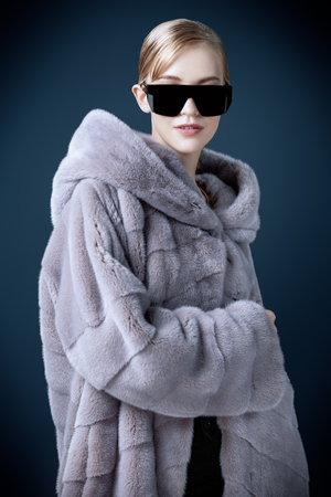 A portrait of a young fashionable woman in a fur coat with hood and sunglasses. Beauty, optics, fashion.の写真素材