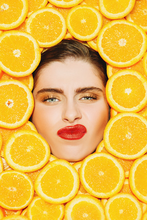 A portrait of a bright beautiful girl with juicy oranges posing in the studio over the yellow background. Beauty, health.の写真素材
