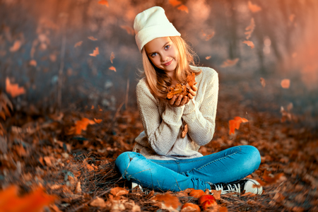 A pretty young girl is sitting on the ground with golden leaves. Autumn fashion, beauty.の写真素材