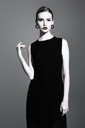 A portrait of a confident lady wearing a black dress and posing in the studio over the grey background. Beauty, make-up, fashion, style.の写真素材
