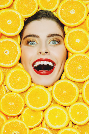 A portrait of a bright laughing beautiful girl with juicy oranges posing in the studio over the yellow background. Beauty, health.の写真素材