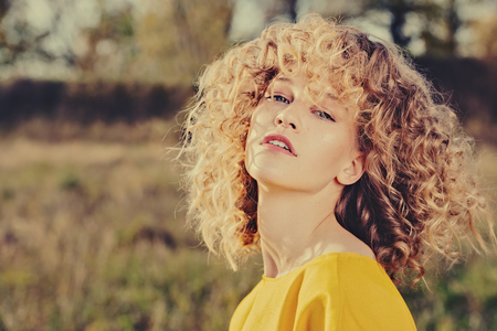 A portrait of a charming young girl with curly fair hair in a yellow dress. Fashion, beauty.の写真素材