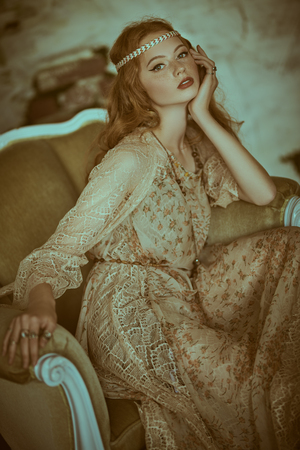 Portrait of a beautiful red-haired young woman sitting in vintage armchair. Hippie style. Bohemian style.の写真素材