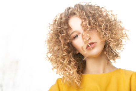 A portrait of a charming young girl with curly fair hair in a yellow dress. Fashion, beauty.の写真素材