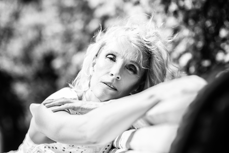 A monochrome portrait of an elderly stylish woman in the summer park on the bench. Beauty, fashion.の写真素材