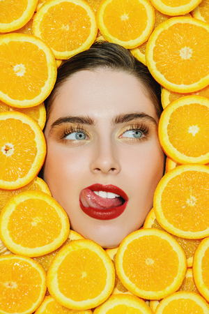A portrait of a bright funny beautiful girl with juicy oranges posing in the studio over the yellow background. Beauty, health.の写真素材