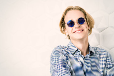 A portrait of a young brutal  man in a checked shirt and sunglasses posing indoor. Men fashion,...