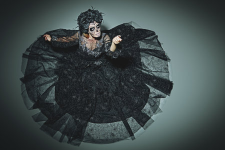 Scary and beautiful Calavera Catrina looking up at camera over dark background. Fashion model with...