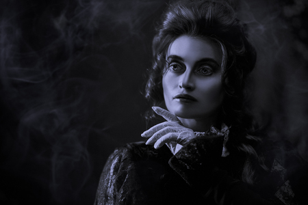 The Victorian era concept. Black-and-white portrait of a beautiful woman in elegant historical dress and hairstyle posing in vintage interior. Baroque. Fashion.の写真素材