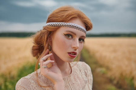Romantic young woman with beautiful red hair walking in a golden wheat field. Beauty, fashion. Modern hippie, bohemian style.の写真素材