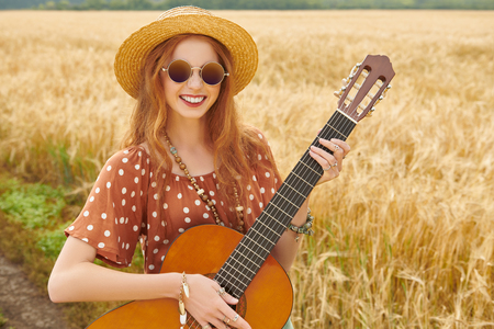 Happy hippie girl stands in a wheat field with her guitar. Spirit of freedom and independence.の写真素材