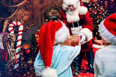 Santa Claus is giving presents to children at home. Merry Christmas and Happy New Year. Miracle...