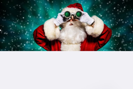 A portrait of Santa Claus looking from behind the white wall with a binocular. Merry Christmas and Happy New Year!の写真素材