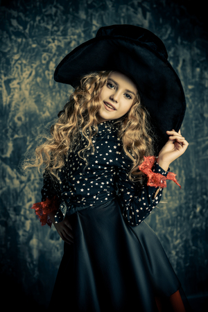 Beautiful child girl in a costume of a witch over grunge background. Halloween party.の写真素材