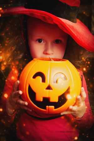 Pretty little girl in a witch costume in the old wooden house with pumpkin. Fairy tales on Halloween.の写真素材