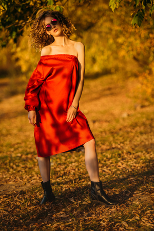 A beautiful young girl is posing in the countryside in a red dress. Fashion concept. Golden autumn.の写真素材