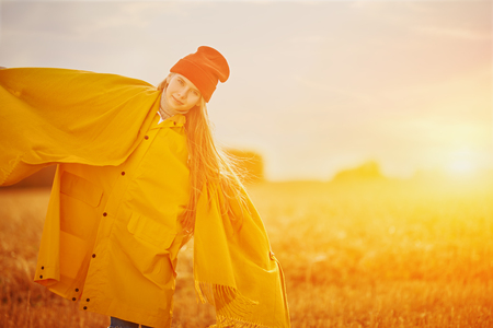 Happy child girl in bright yellow raincoat stands in autumn field. Seasonal fashion. Autumn.の写真素材