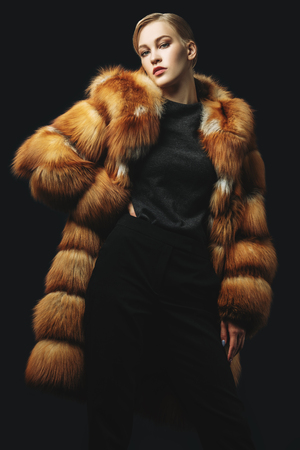 A portrait of a young fashionable woman in a fur coat with a hood. Beauty, fashion.の写真素材