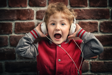 A portrait of a young schoolboy posing in the studio over the brick wall and listening to music in the headphones. Kids casual fashion, education.の写真素材