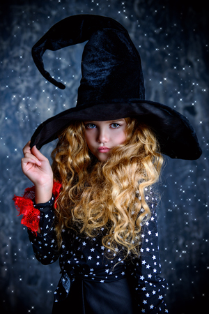 Beautiful child girl in a costume of a witch over grunge background. Halloween party.の写真素材