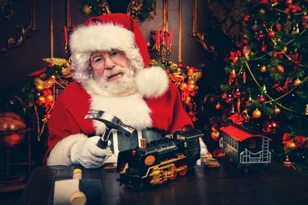 Santa Claus is sitting at a table at home making gifts. Merry Christmas and Happy New Year. Miracle time.の写真素材