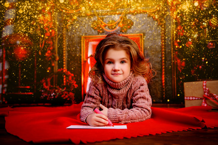 A happy girl is lying in the floor in the room decorated for Christmas and writing a wish letter to Santa. Christmas, New Year.の写真素材