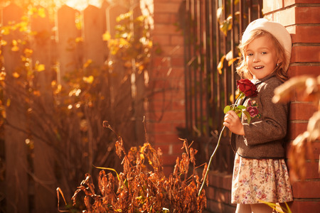 Cute little girl with a red rose walks in the autumn park. Retro style. Children's fashion.の写真素材