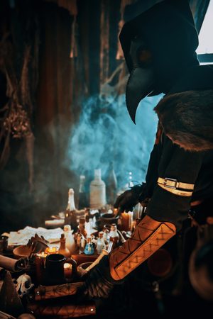 The plague doctor is working at his desk, inventing a cure for bubonic plague. The atmosphere of mysticism. Historical reenactment. Halloween.の写真素材