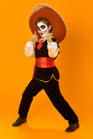 Portrait of a handsome boy with sugar skull makeup over bright yellow background. Halloween. Dia de los muertos. Day of the dead. Copy space. Full length portrait.の写真素材