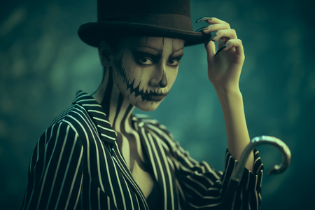 Elegant young woman in a male tailcoat and top-hat with pumpkin skull make-up. Pumpkin queen. Costumes and makeup for Halloween.の写真素材