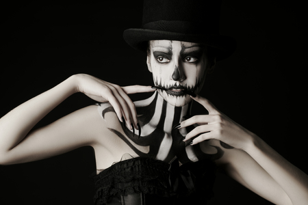 Elegant young woman in a male top-hat with pumpkin skull make-up over black background. Pumpkin queen. Costumes and makeup for Halloween. Copy space.の写真素材