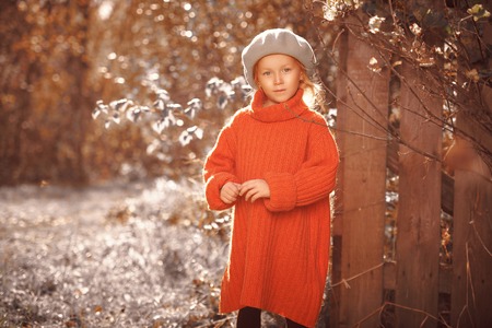 Autumn beauty. Little girl with golden hair stands in the sun in a beautiful autumn park. Children's fashion.の写真素材