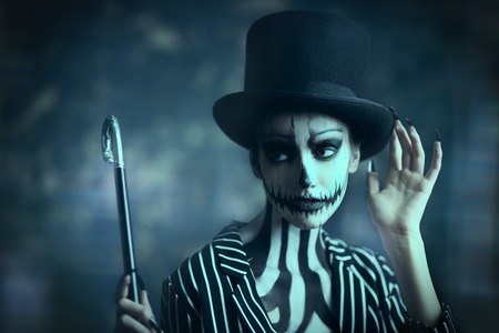 Elegant young woman in a male tailcoat and top-hat with pumpkin skull make-up. Pumpkin queen. Costumes and makeup for Halloween.の写真素材