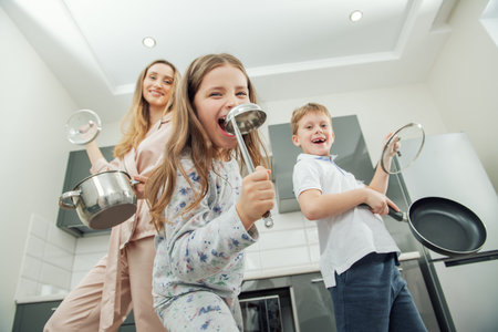 Young woman and her children are funing  with the kitchen utensils in the kitchen. Family home shoot.の写真素材