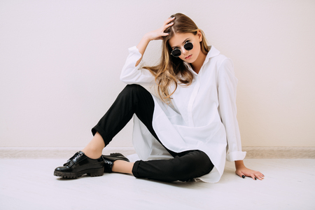 Portrait of a cute girl teenager with sunglasses sitting on the floor in the room. Glasses for a modern young generation. Beauty, fashion.の写真素材