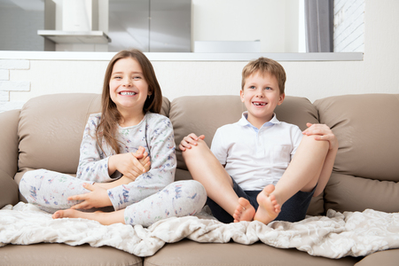 Cute boy and girl are  sitting on the couch.  Fashion home shot. Childhood. Kid's fashion.の写真素材