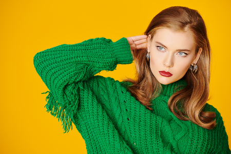Portrait of an attractive young woman in green sweater over yellow background. Beauty, make-up and cosmetics concept.の写真素材